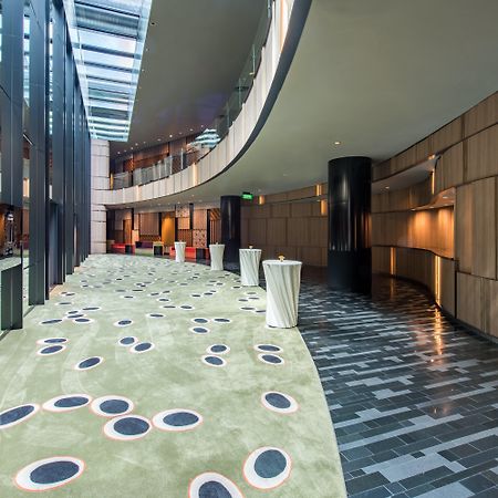 Crowne Plaza Changi Airport, An Ihg Hotel Singapore Exterior photo The photo shows a modern indoor space that features a curved hallway with a mix of materials and textures. The floor is divided into two sections: one has a smooth, dark tiled design, while the other has a soft, green carpet with circular patterns in