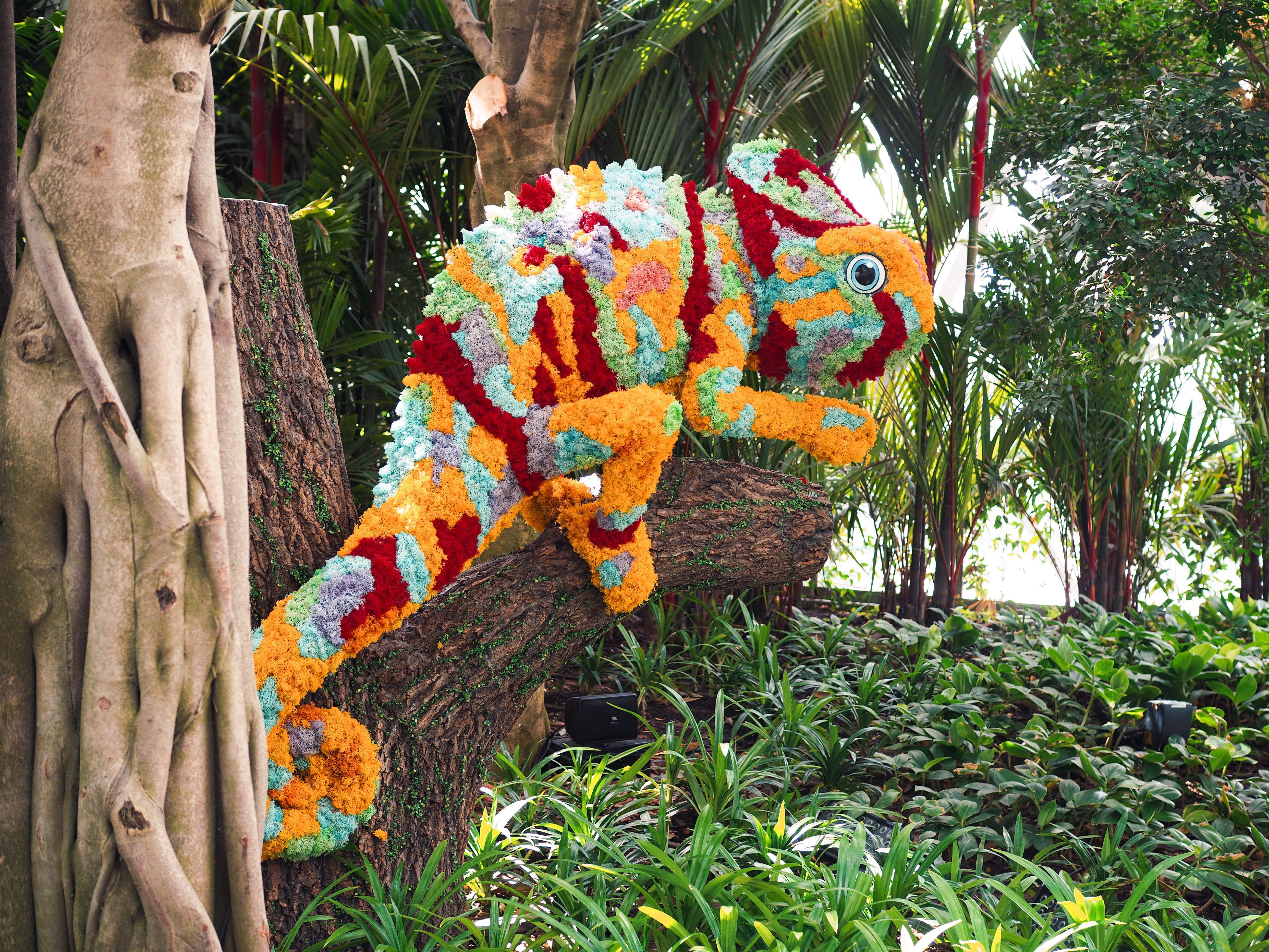 Crowne Plaza Changi Airport, An Ihg Hotel Singapore Exterior photo The photo shows a vibrant and colorful chameleon sculpture made from flowers and plant materials. The chameleon is positioned on a tree trunk, blending in with the lush greenery of its surroundings. The colors of the sculpture include shades of orang