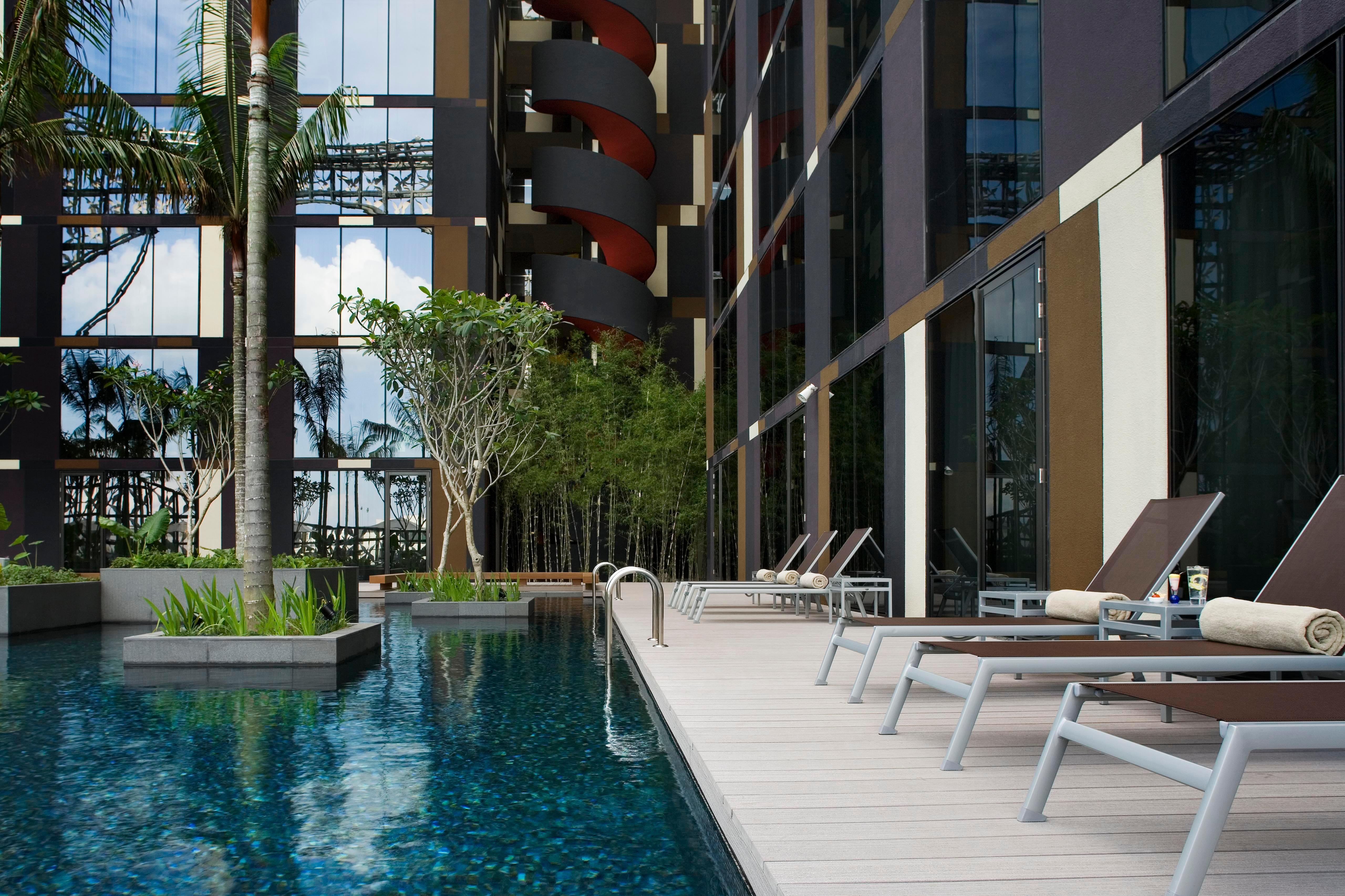 Crowne Plaza Changi Airport, An Ihg Hotel Singapore Facilities photo The photo shows a modern swimming pool area adjacent to a building. The pool is surrounded by sleek wooden decking and features a clear blue water surface. There are several lounge chairs positioned around the pool for relaxation. Lush greenery, incl