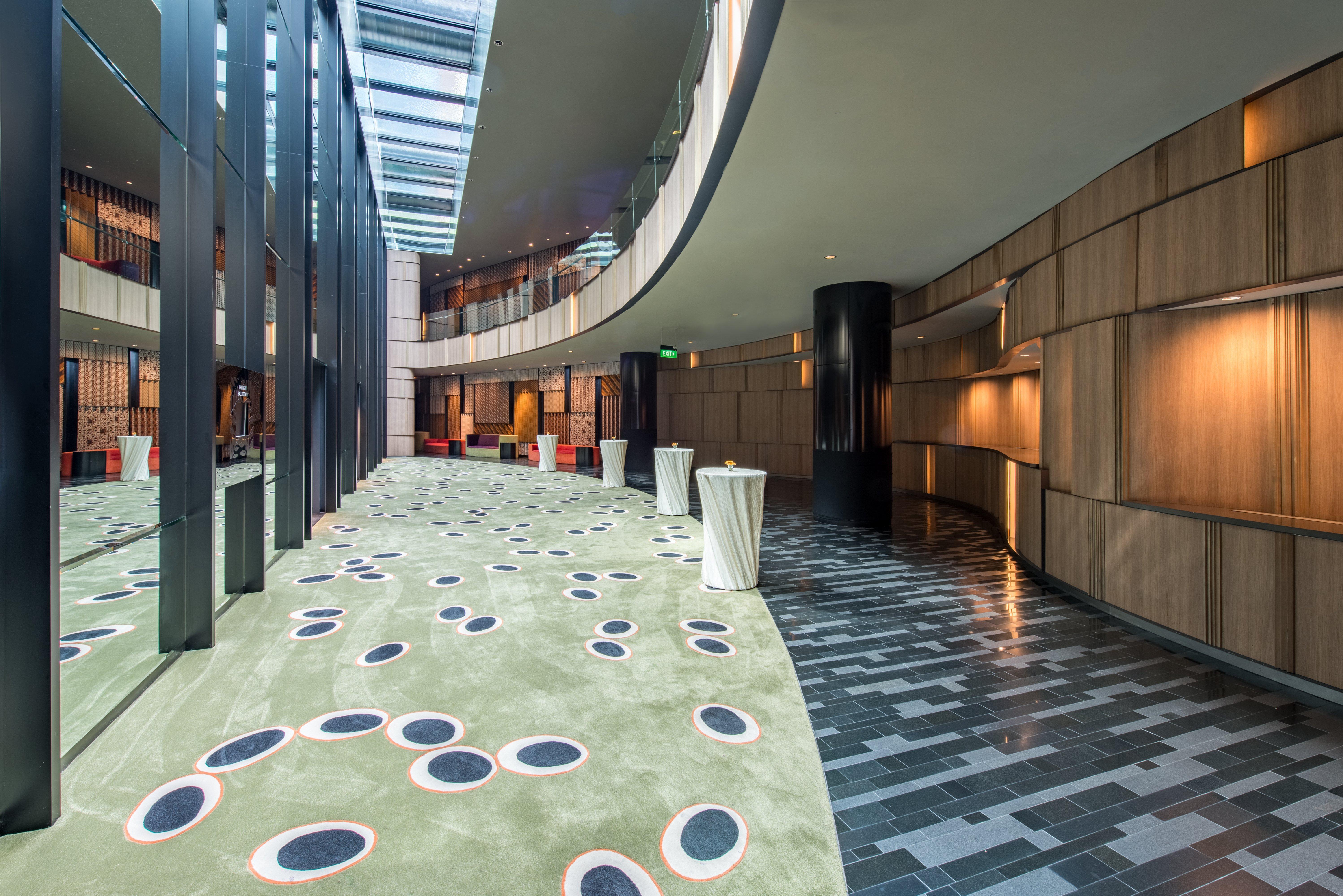 Crowne Plaza Changi Airport, An Ihg Hotel Singapore Exterior photo The photo shows a modern indoor space that features a curved hallway with a mix of materials and textures. The floor is divided into two sections: one has a smooth, dark tiled design, while the other has a soft, green carpet with circular patterns in