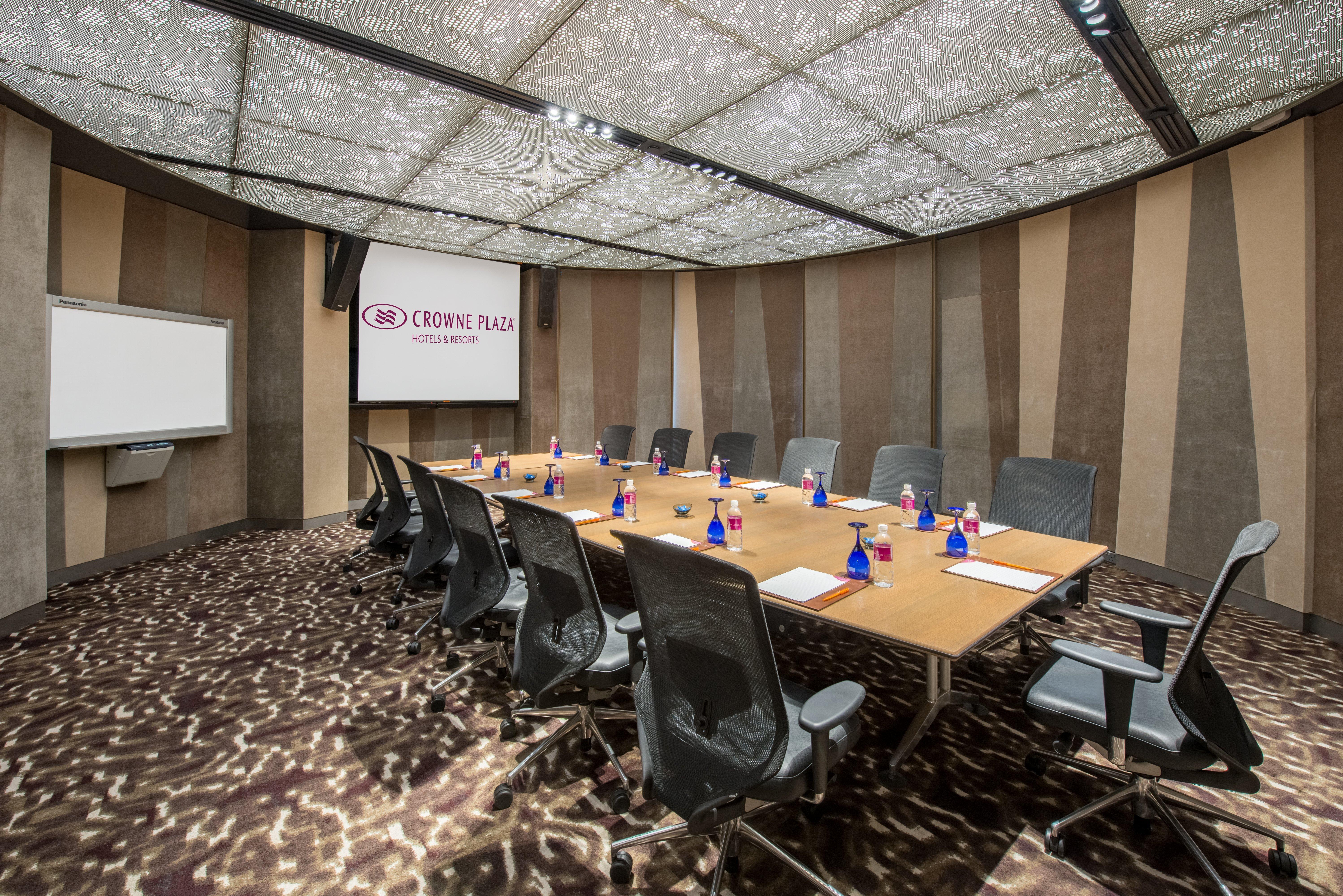 Crowne Plaza Changi Airport, An Ihg Hotel Singapore Exterior photo The photo shows a modern conference room. It features a large, rectangular wooden table surrounded by ergonomic black office chairs. On the table, there are small blue vases, each containing flowers. The room has a unique, patterned ceiling that enha