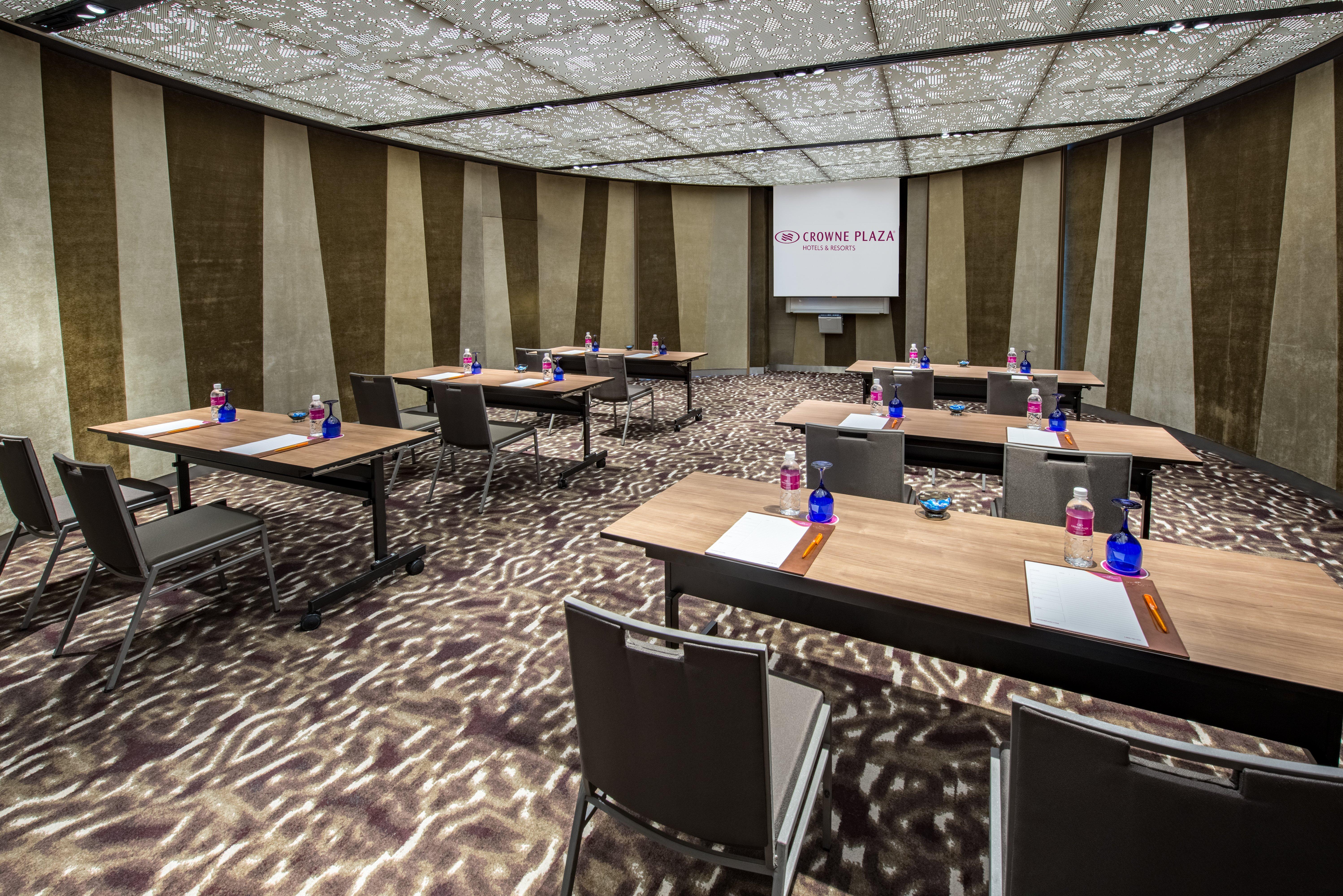 Crowne Plaza Changi Airport, An Ihg Hotel Singapore Exterior photo The photo shows a modern conference room set up for a meeting or presentation. There are several wooden tables arranged in a U-shape, each equipped with a notepad and pen. Bottled water is placed in blue containers on the tables. The room features a 