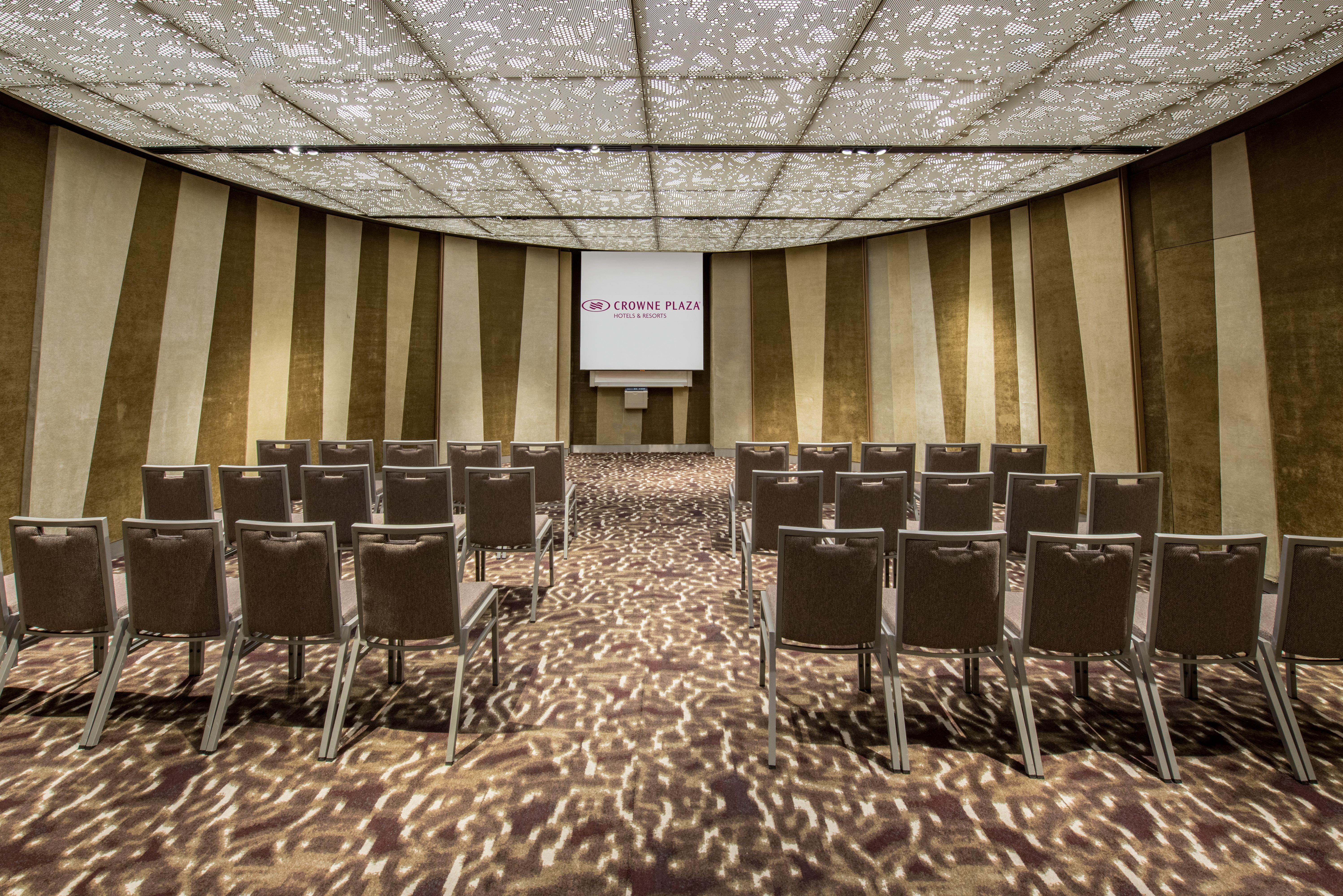 Crowne Plaza Changi Airport, An Ihg Hotel Singapore Exterior photo The photo shows a conference or meeting room. It features rows of grey chairs arranged in a semi-circular layout, facing a screen at the front. The room has a decorative ceiling with a patterned design that allows light to filter through, creating in