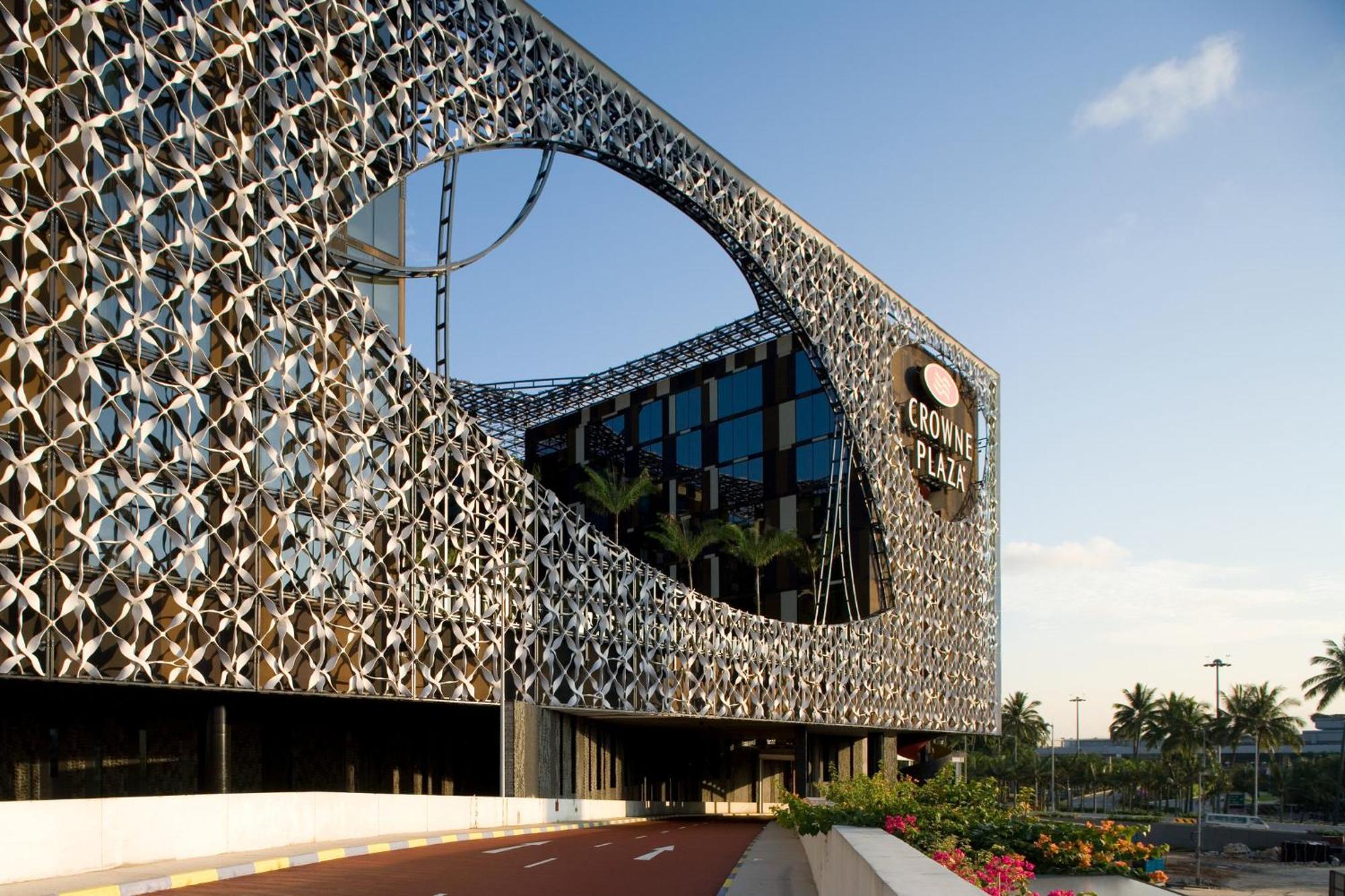 Crowne Plaza Changi Airport, An Ihg Hotel Singapore Exterior photo The photo features a modern building with a unique architectural design. The facade consists of a complex lattice structure that creates a visual pattern, including a large circular cutout. The building appears to be multi-story, with large glass win