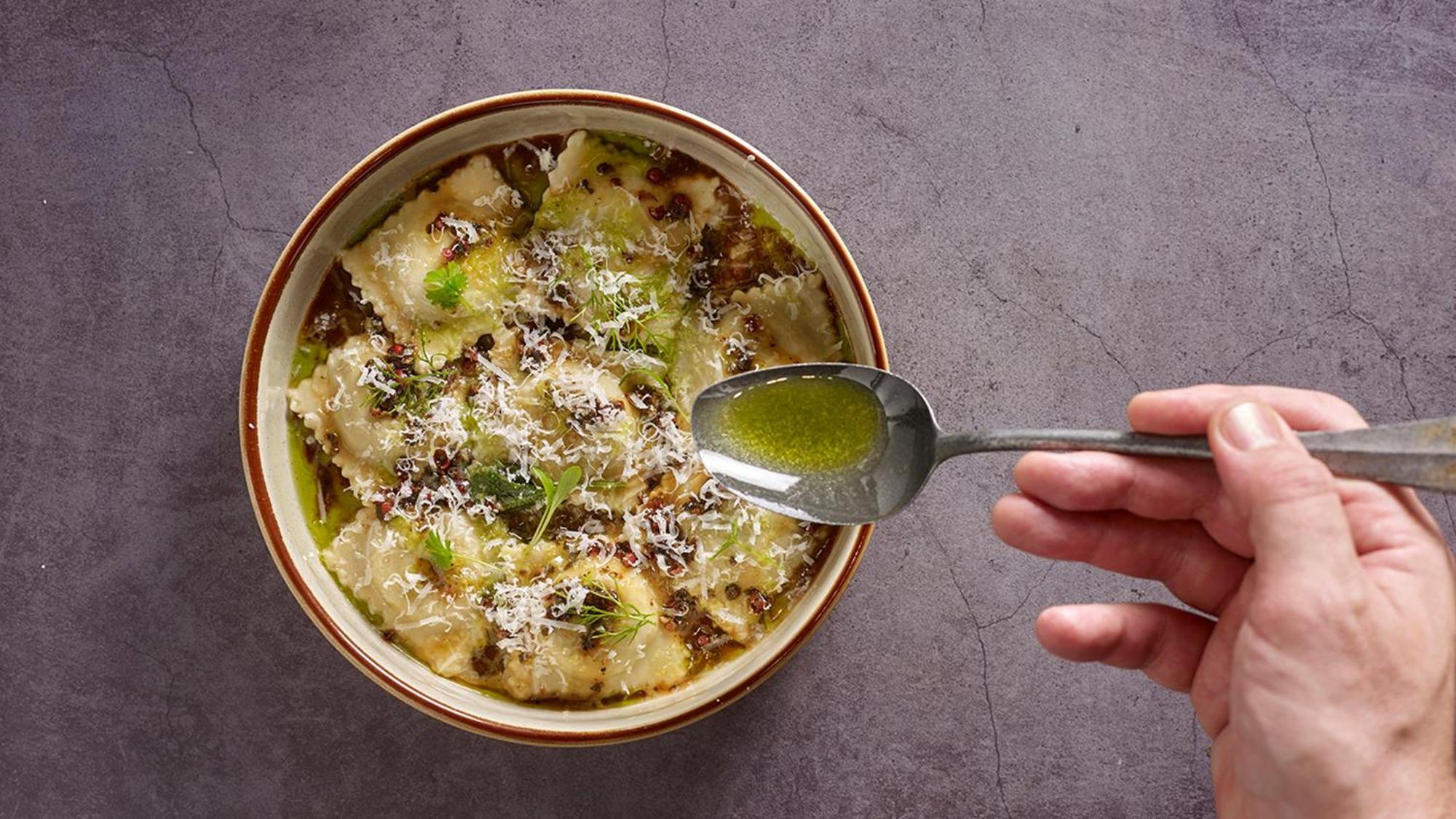 Crowne Plaza Changi Airport, An Ihg Hotel Singapore Exterior photo The photo shows a bowl of ravioli garnished with grated cheese and drizzled with olive oil. A hand is holding a spoon above the bowl, indicating the action of adding more oil or sauce. The dish appears delicious and is presented with an appealing aes