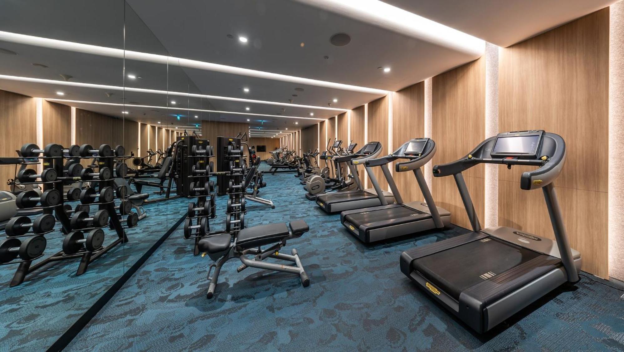 Crowne Plaza Changi Airport, An Ihg Hotel Singapore Exterior photo The photo shows a well-equipped gym or fitness room. On one side, there are several weightlifting benches along with dumbbells arranged on racks. On the other side, there are multiple treadmills lined up, suggesting a space designed for both strength