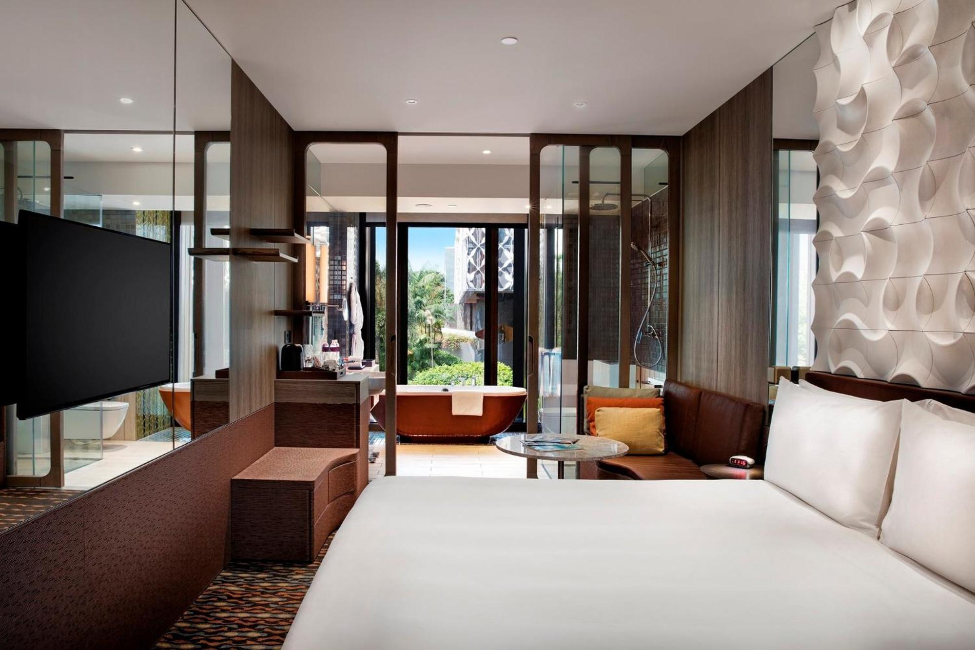 Crowne Plaza Changi Airport, An Ihg Hotel Singapore Exterior photo The photo shows a modern hotel room with a contemporary aesthetic. It features a large bed with white linens positioned against a textured wall. There is a flat-screen TV mounted on the wall and a cozy seating area with a small table and chairs. The 