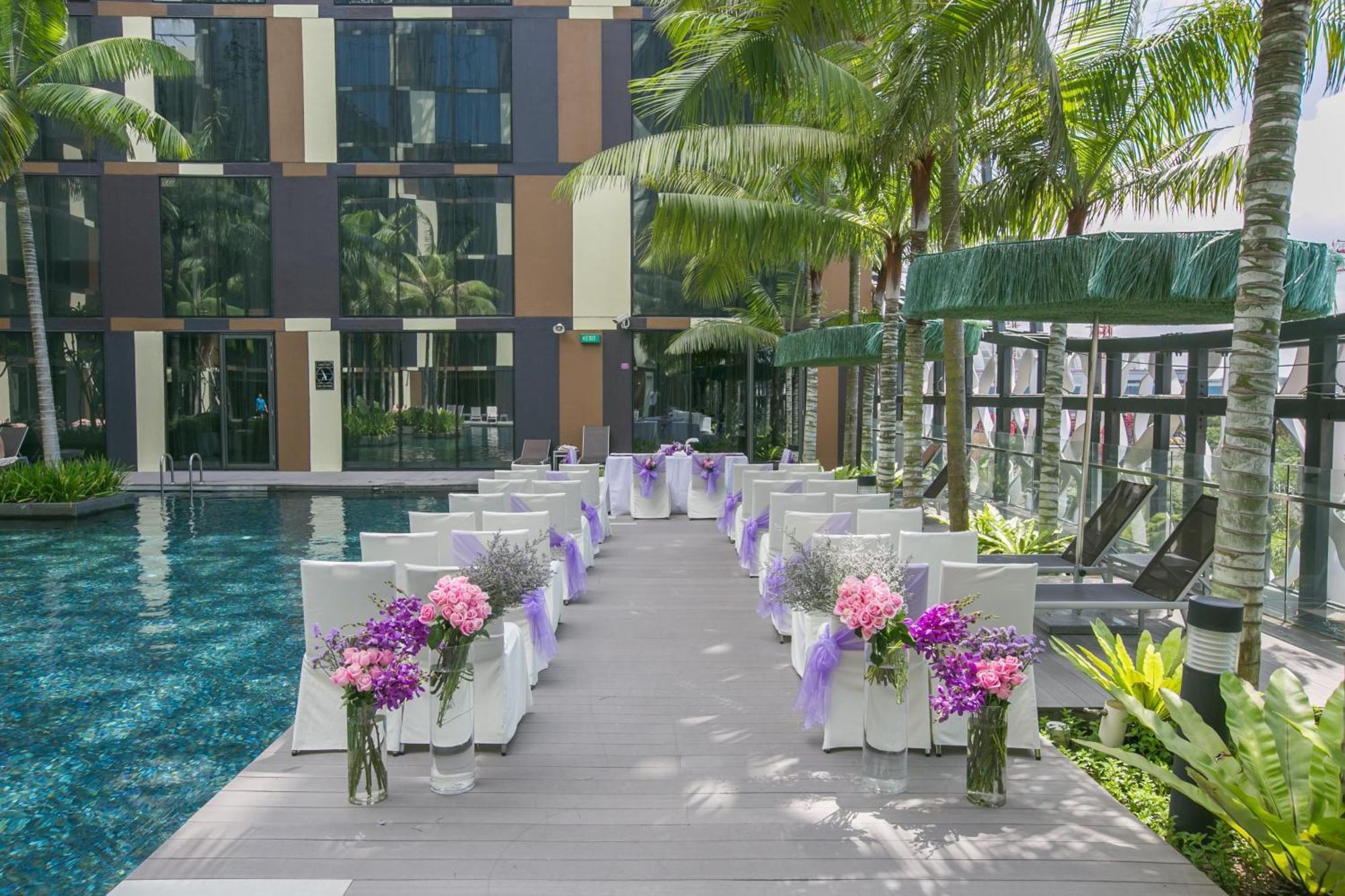 Crowne Plaza Changi Airport, An Ihg Hotel Singapore Exterior photo The photo shows a beautifully arranged outdoor setting for a wedding or a similar event. There is a long aisle made of wooden planks leading to a pool area, flanked by neatly arranged chairs. Each chair is adorned with purple ribbons and decorated wi