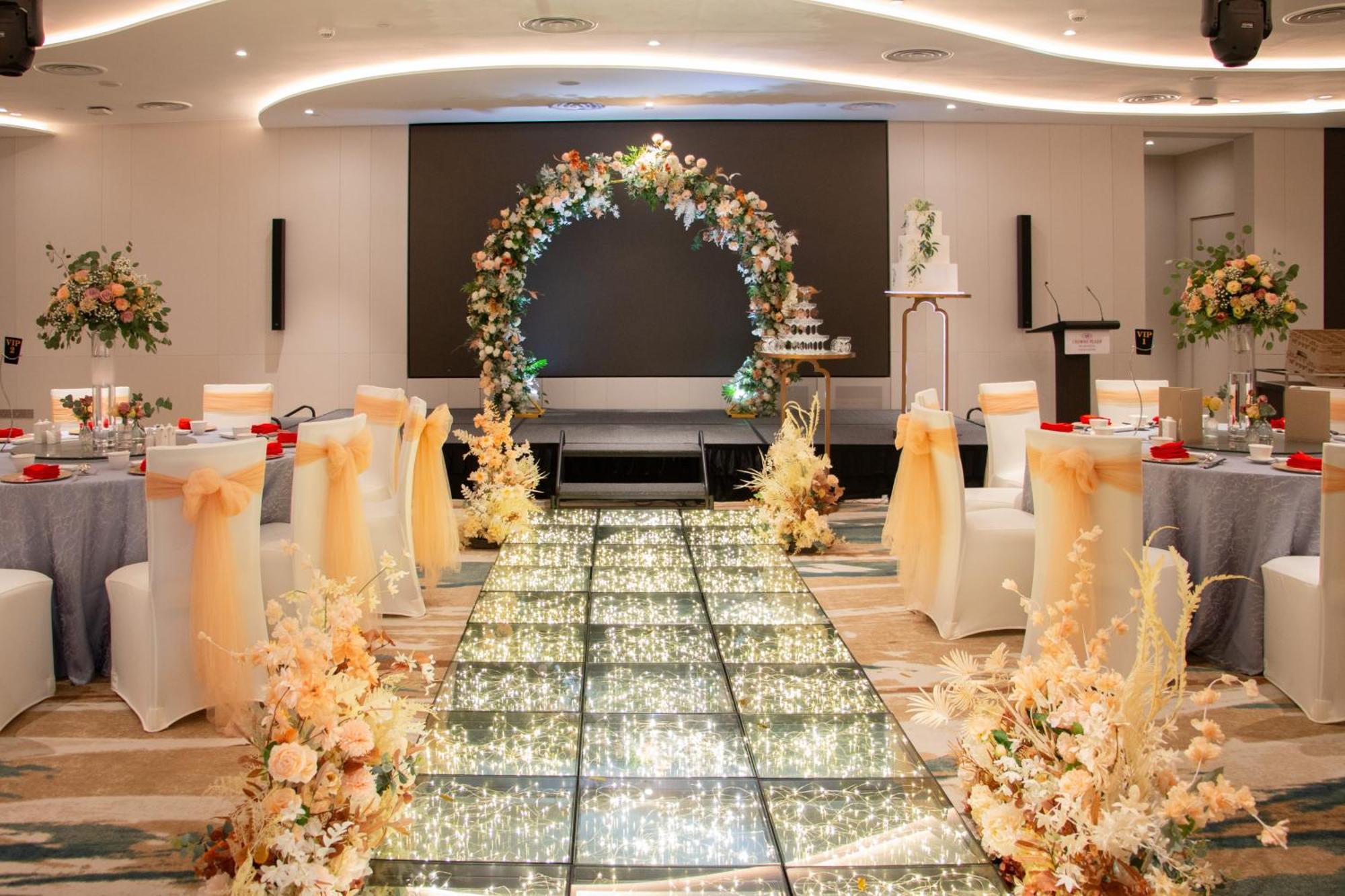 Crowne Plaza Changi Airport, An Ihg Hotel Singapore Exterior photo The image depicts an elegantly decorated event space, likely for a wedding or formal occasion. In the center, there is a flower-adorned archway in warm colors, creating a focal point. A sparkling, illuminated pathway leads towards the arch, bordered 