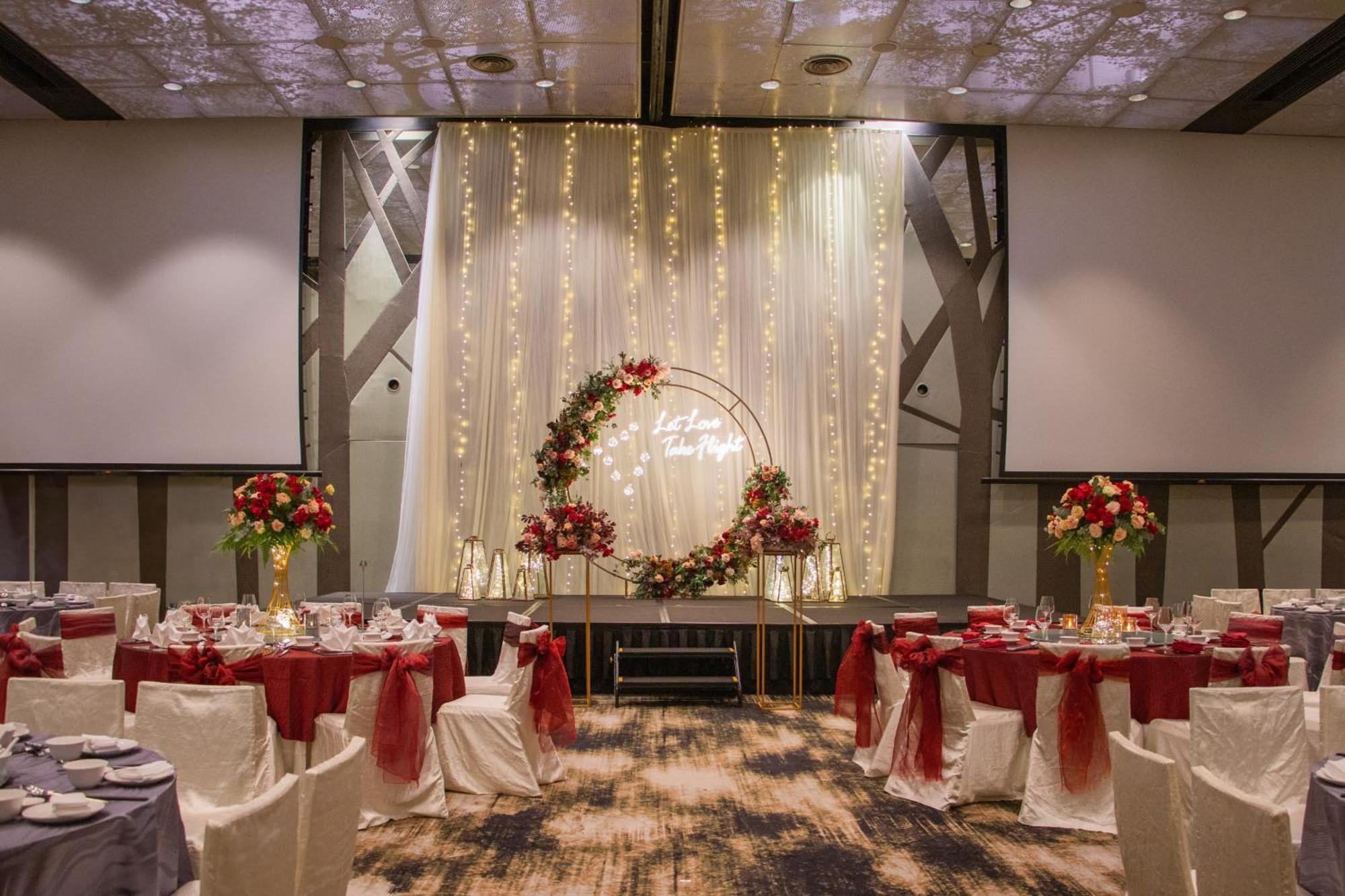 Crowne Plaza Changi Airport, An Ihg Hotel Singapore Exterior photo The photo shows an elegantly decorated banquet hall set up for an event. There are round tables with white tablecloths, each adorned with a red centerpiece. The chairs have white covers and are draped with red sashes. At the back of the room, there i