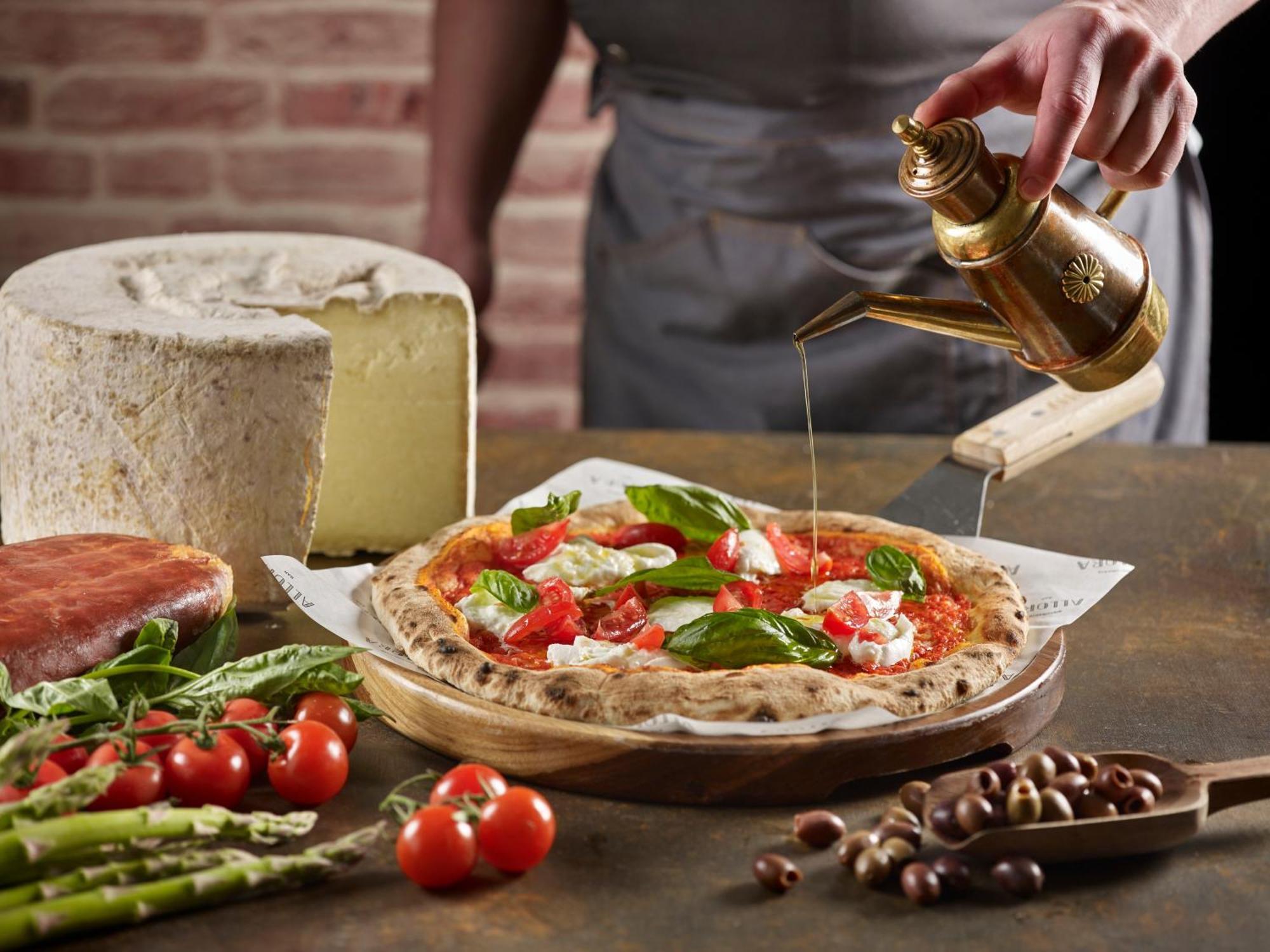 Crowne Plaza Changi Airport, An Ihg Hotel Singapore Exterior photo The photo features a freshly made pizza being drizzled with oil. The pizza is topped with ingredients such as fresh basil and tomatoes, and has a golden, crispy crust. In the background, there is a block of cheese and a piece of ham. Surrounding the 