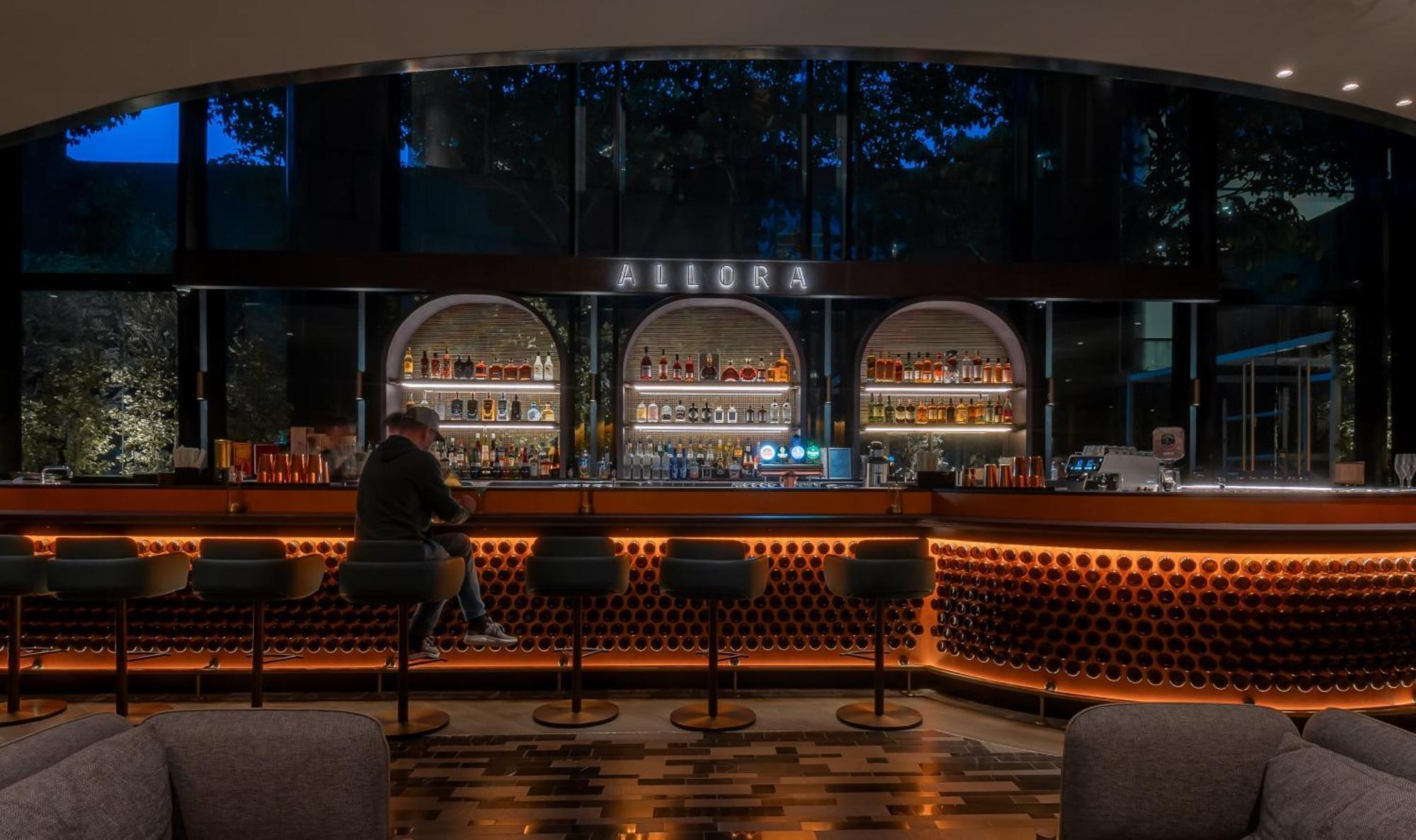 Crowne Plaza Changi Airport, An Ihg Hotel Singapore Exterior photo The photo shows a bar area with a modern and stylish design. In the center, there is a well-lit bar counter featuring a variety of alcoholic beverages displayed on shelves behind it. The bar has a sleek, contemporary look with circular light fixtures