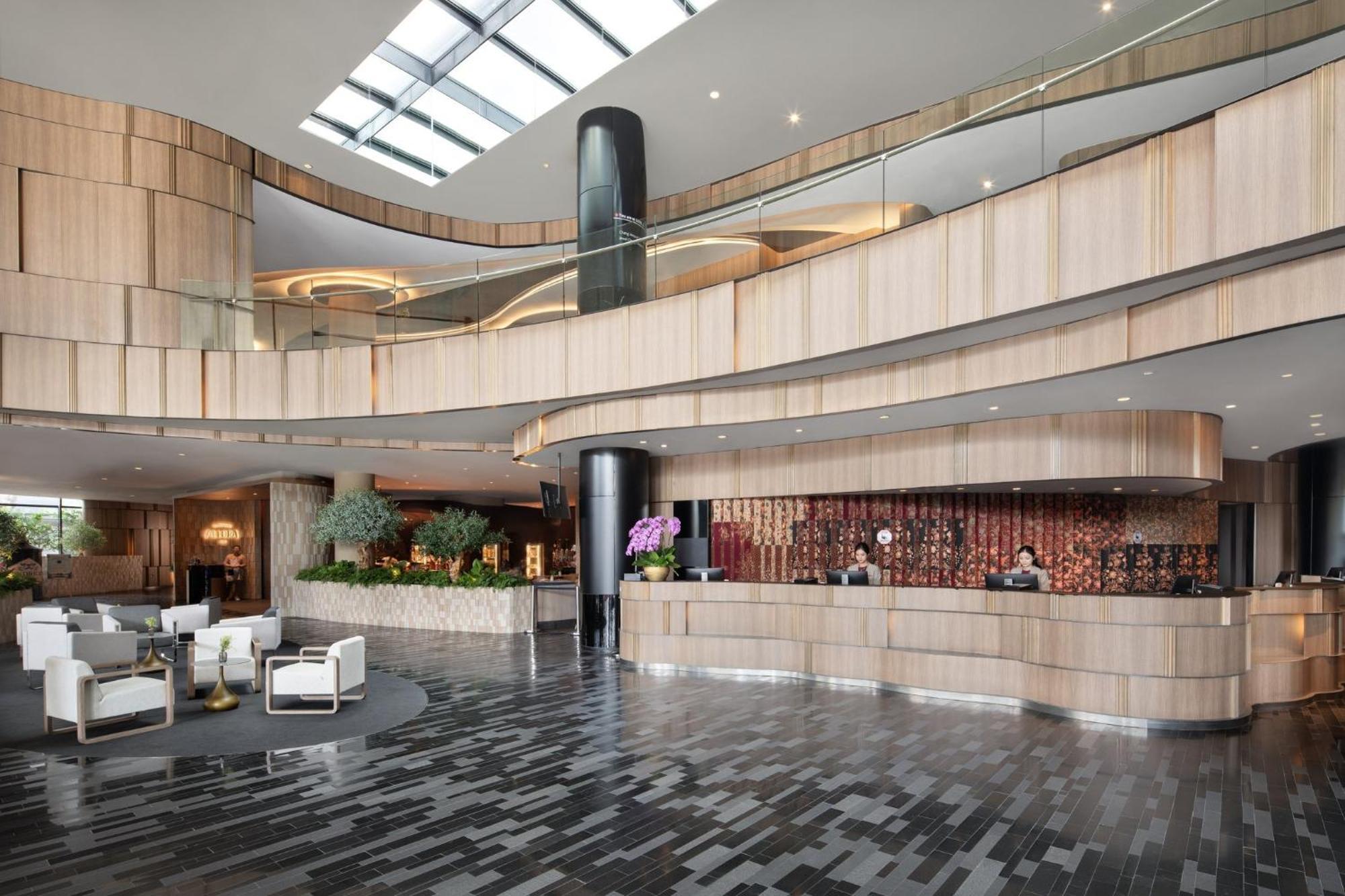 Crowne Plaza Changi Airport, An Ihg Hotel Singapore Exterior photo The photo shows a modern hotel lobby with a sleek and stylish design. The reception area features a curved wooden counter, with staff members attending to guests. The interior design includes a mix of wood and stone materials, creating a warm and inv